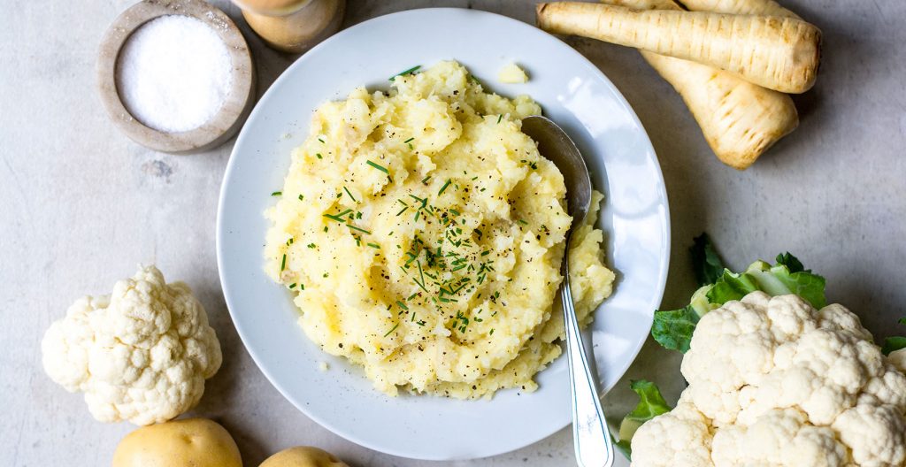 mashed potatoes in bowl with cauliflower and potatoes around it